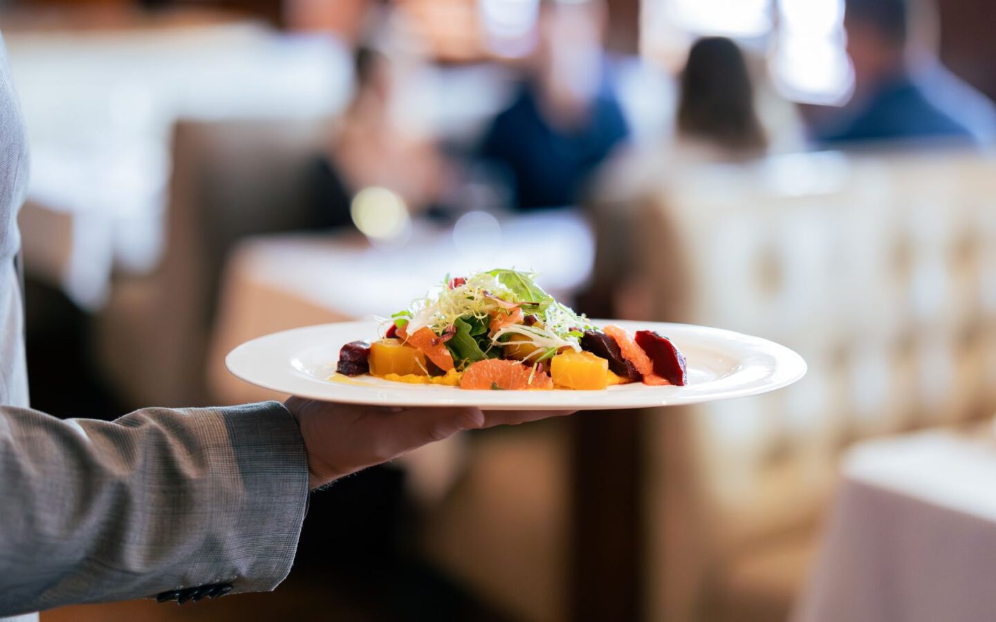 Server holding a plated salad in a fine-dining restaurant.