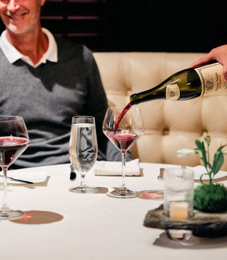 Red wine being poured at a romantic restaurant table.