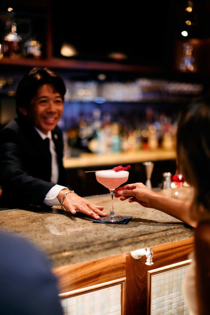Bartender passing a pink cocktail to a guest across a polished bar counter
