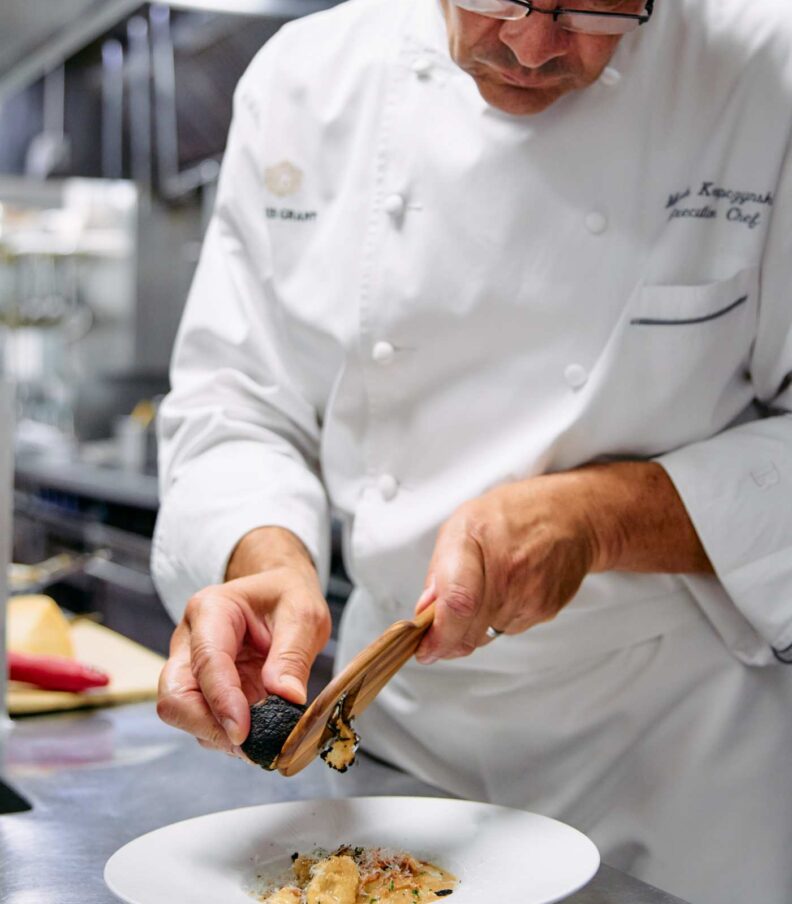 Chef finishing a plated pasta dish by grating fresh truffle in a professional kitchen