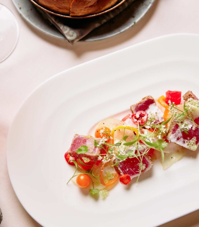 Plated fine dining dish with seared tuna, sliced vegetables, herbs, and sauce on a white plate