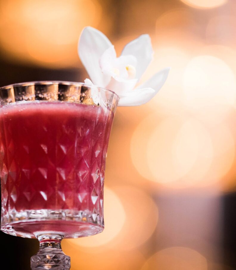 Red cocktail in patterned glass with white flower garnish