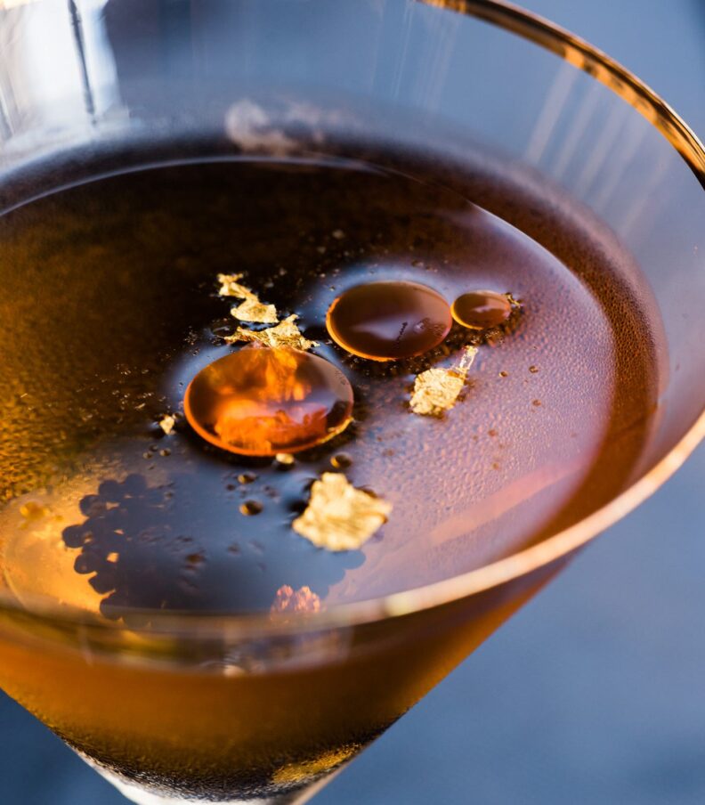 Dark cocktail in martini glass with gold leaf garnish