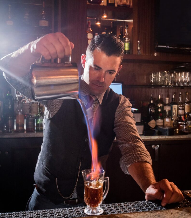 Bartender pouring flaming cocktail behind bar