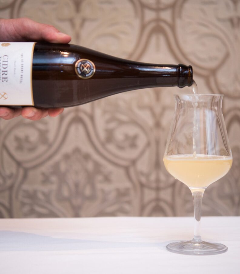 Hand pouring sparkling cider from a bottle into a stemmed glass on a white table