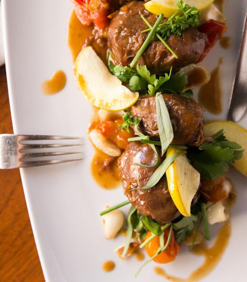 Plated fine dining dish with seared meat, vegetables, herbs, and sauce on a white rectangular plate