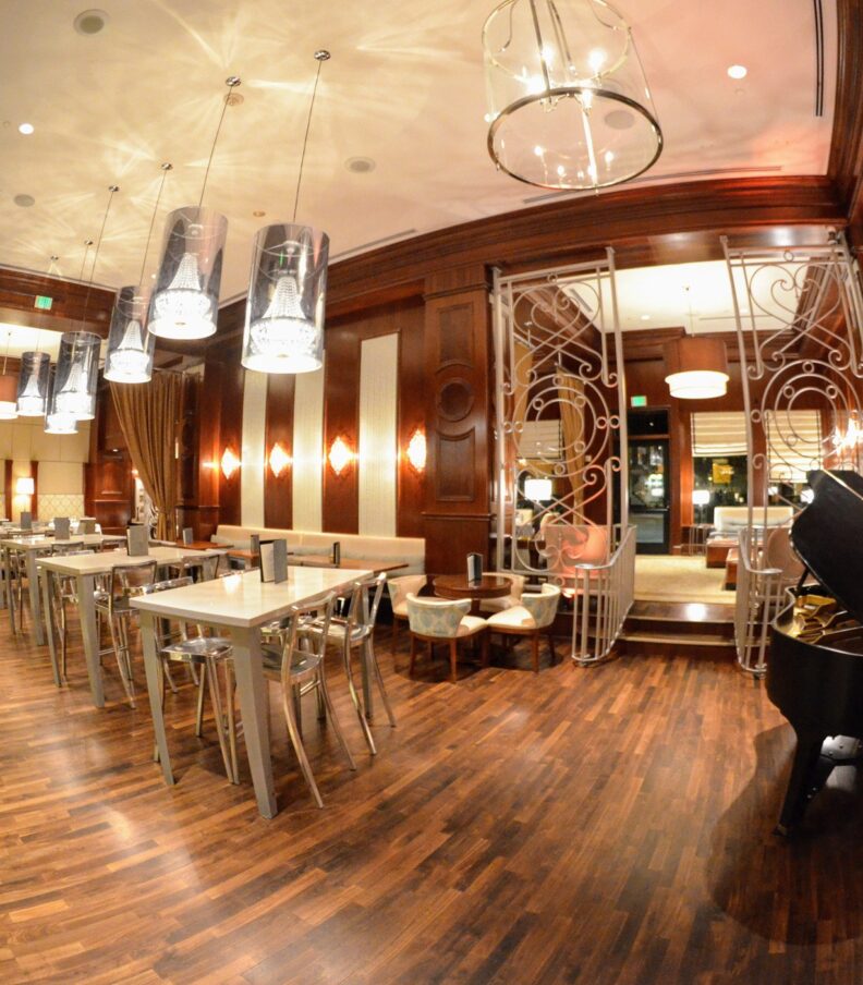Wide angle view of an elegant restaurant dining room with wood floors, modern tables, pendant lighting, and a grand piano