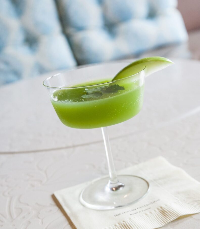 a green cocktail garnished with a wedge of lime