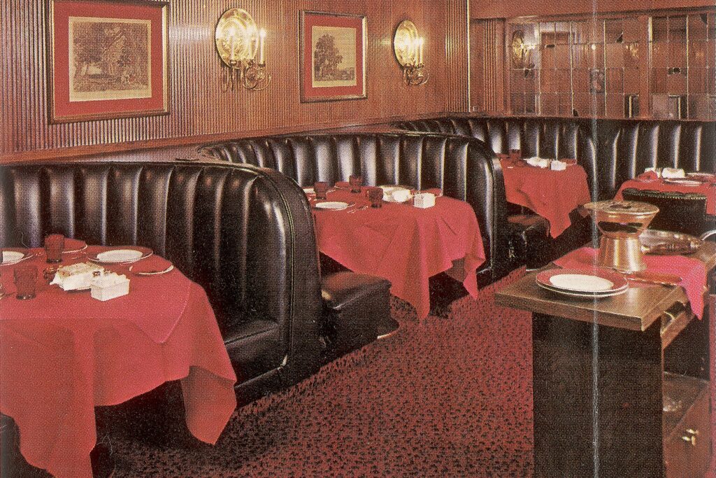 Vintage restaurant dining booths with red tablecloths, black leather seating, framed wall art, and warm ambient lighting.