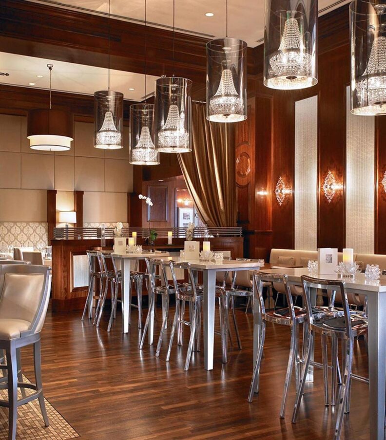 Upscale restaurant interior with wood paneling, high tables, bar seating, and pendant lights in an elegant dining room.