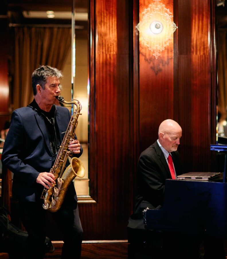 Jazz musicians performing inside the restaurant with saxophonist standing beside a pianist at a grand piano