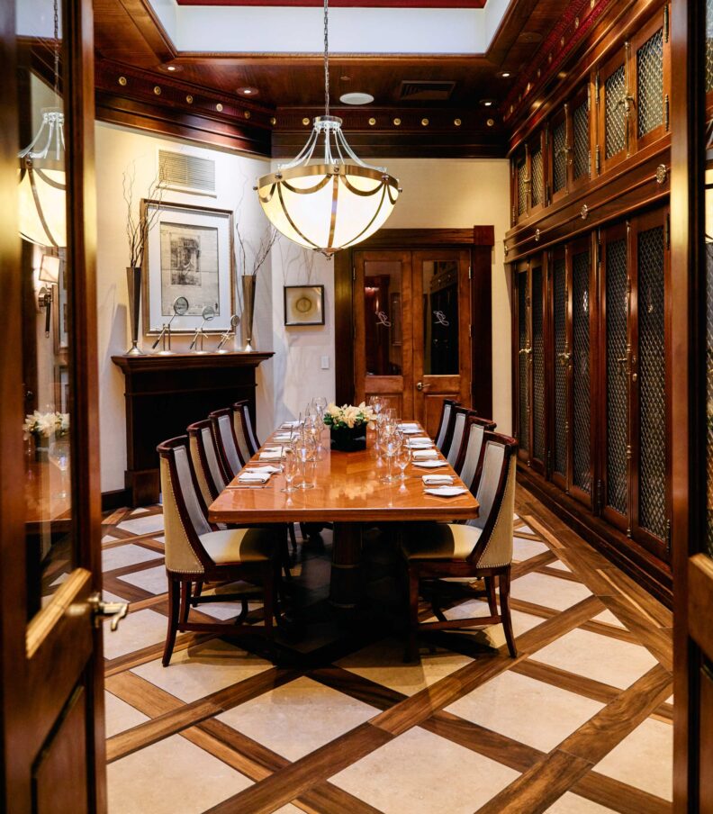 Private dining room with long wooden table, upholstered chairs, chandelier lighting, and wood paneled walls