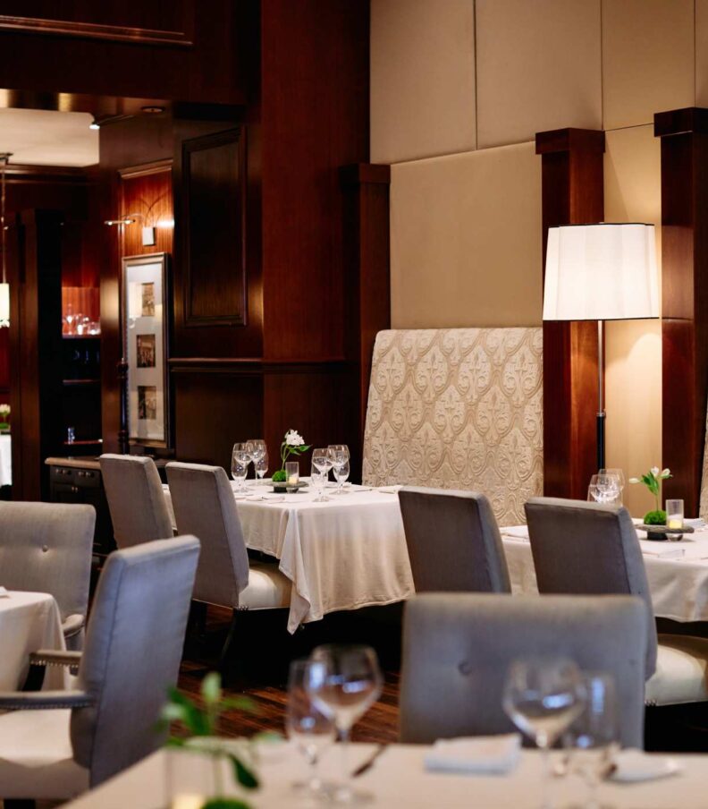 Elegant dining room with white tablecloth tables, upholstered chairs, and warm wood paneling