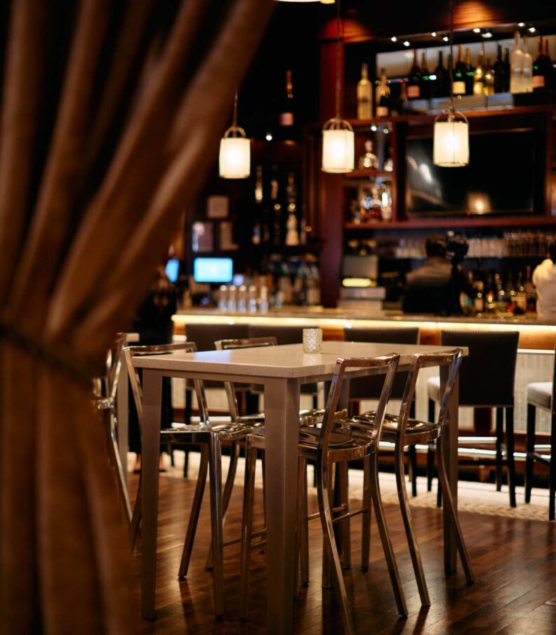 High top table with metal chairs near a softly lit restaurant bar interior