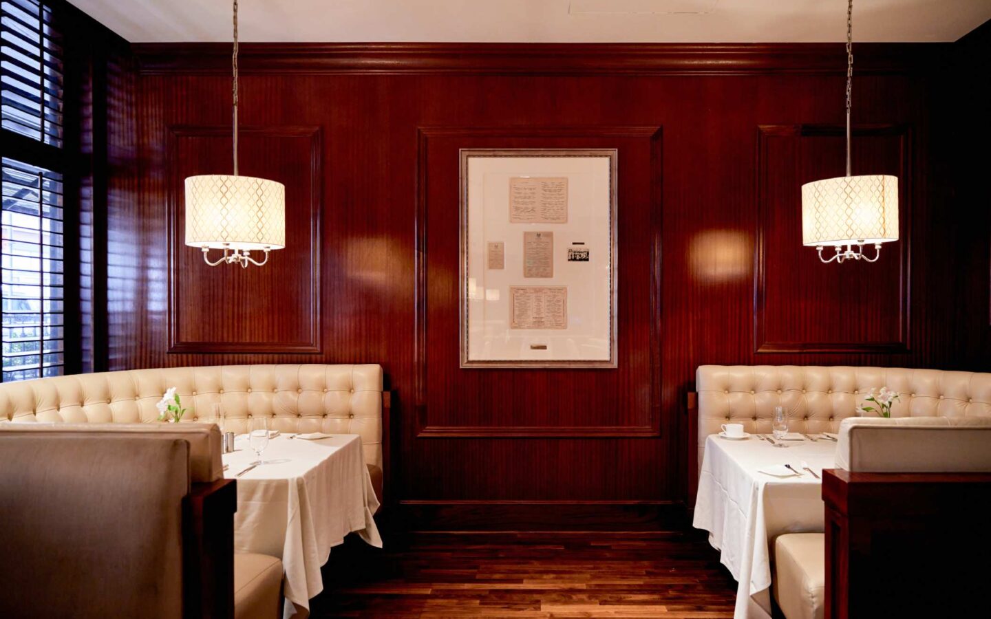 Classic restaurant booths with white tablecloths, upholstered seating, and warm wood paneling under soft pendant lighting