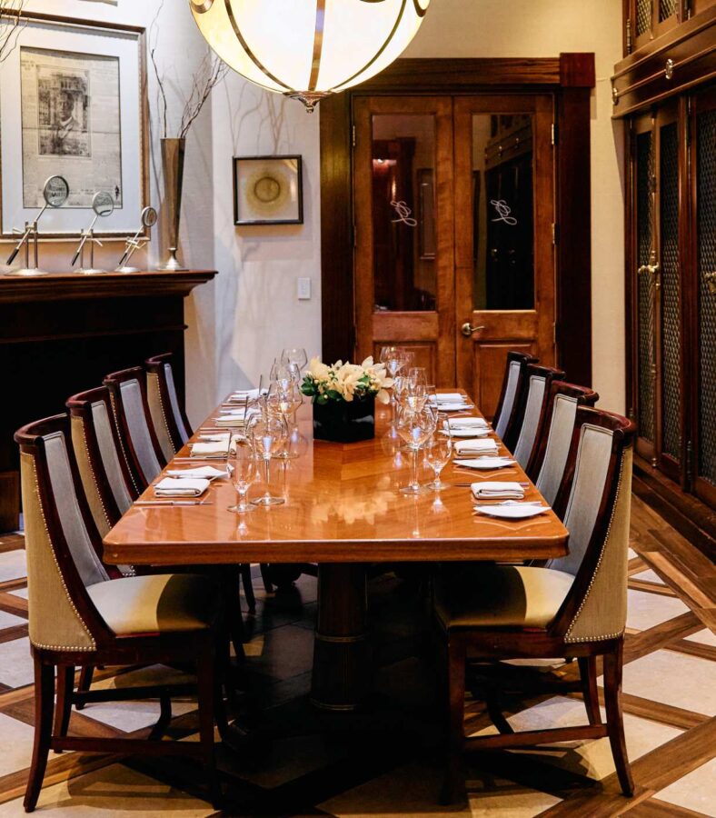 Private dining room with a long set table, wine glasses, and upholstered chairs in an elegant restaurant setting
