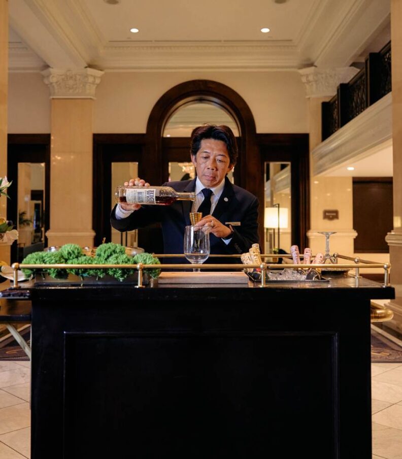 Bartender preparing a cocktail at a mobile bar station in an elegant hotel lobby setting